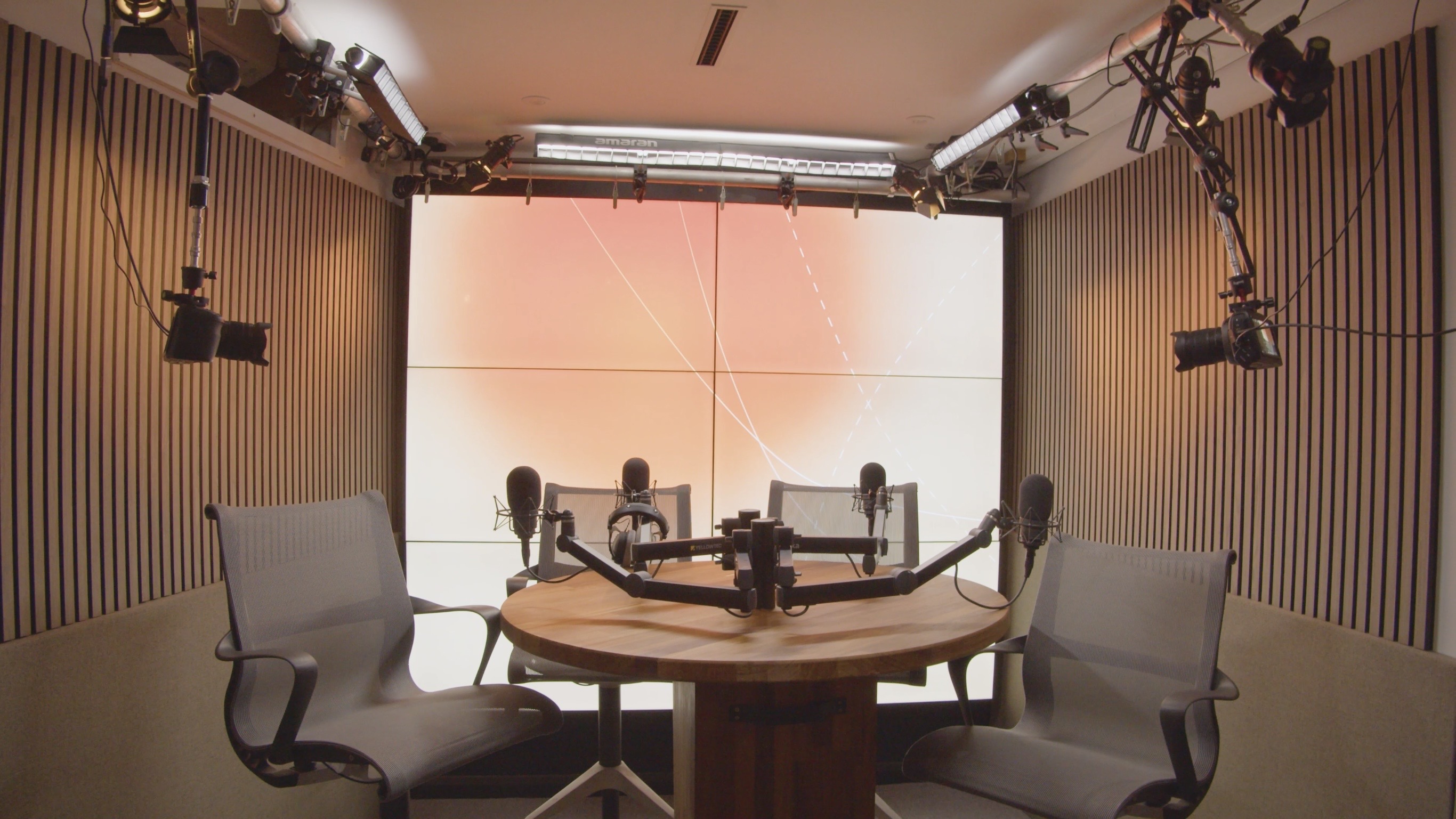 Professional recording studio London featuring 6-TV background and roundtable podcast setup with four chairs and four Neumann microphones.