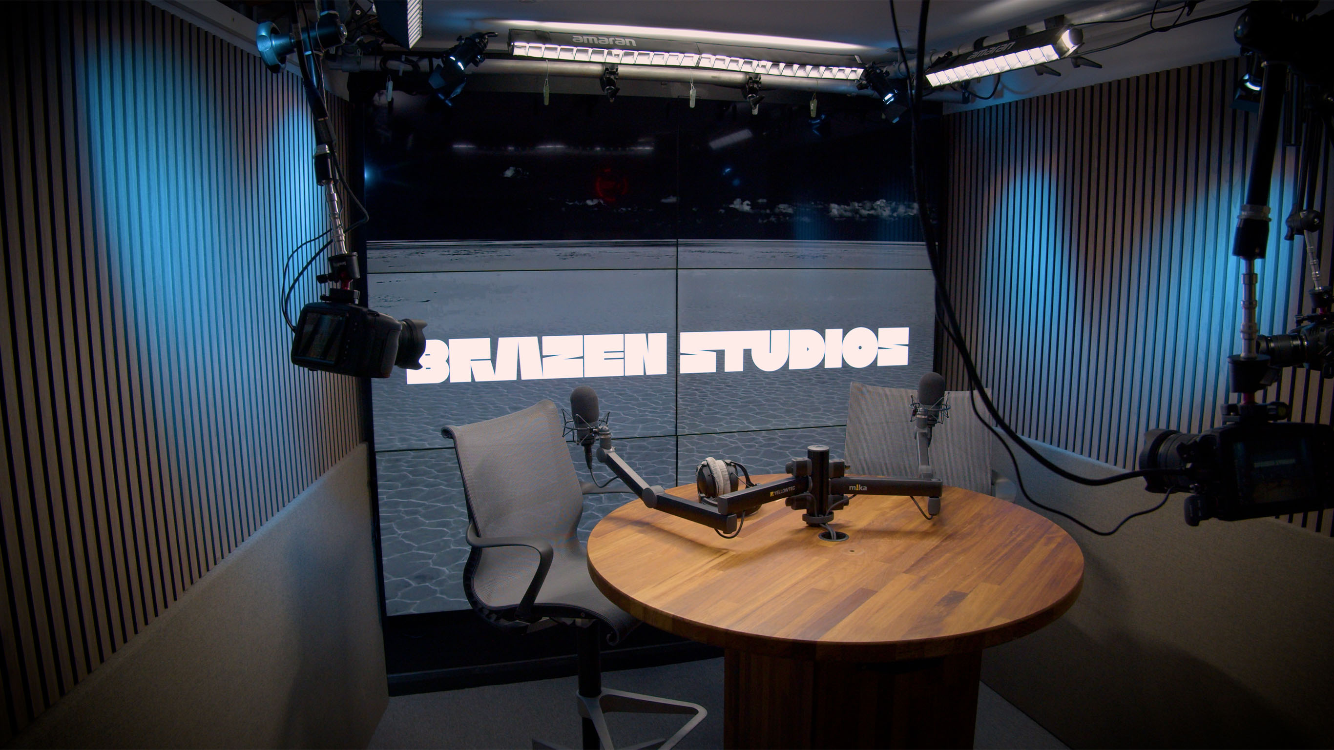 Brazen Studios iconic 6-TV background with intimate two-person roundtable setup, ideal for interview-style video recording studio sessions.